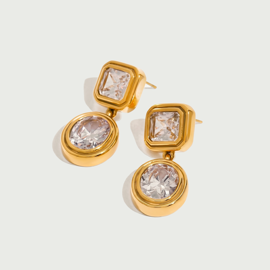 A pair of gold-tone drop earrings, each with a square crystal stud and a round crystal drop, on a plain background