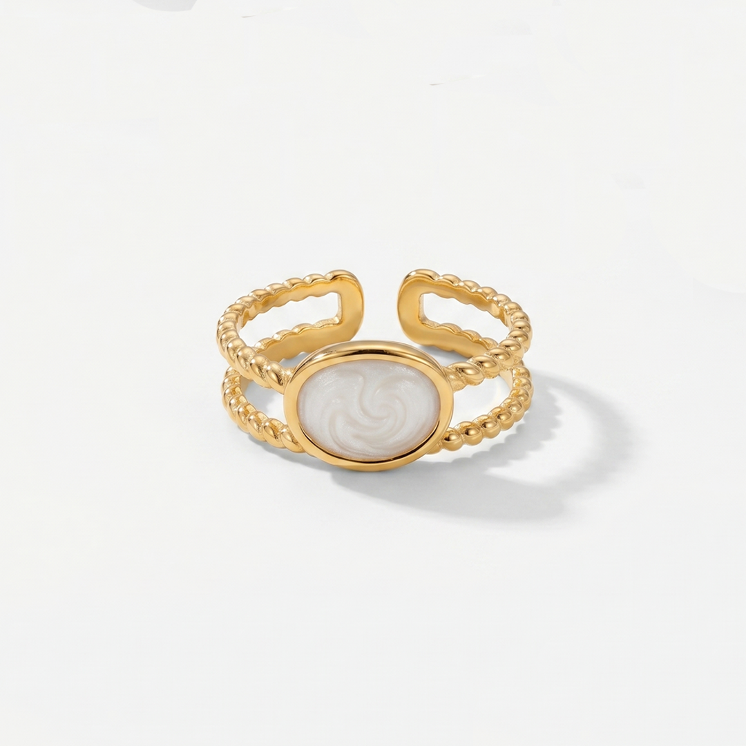 A gold-tone open ring with a pearlescent white oval between two textured bands, on a plain background