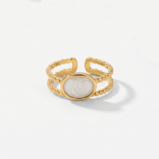A gold-tone open ring with a pearlescent white oval between two textured bands, on a plain background