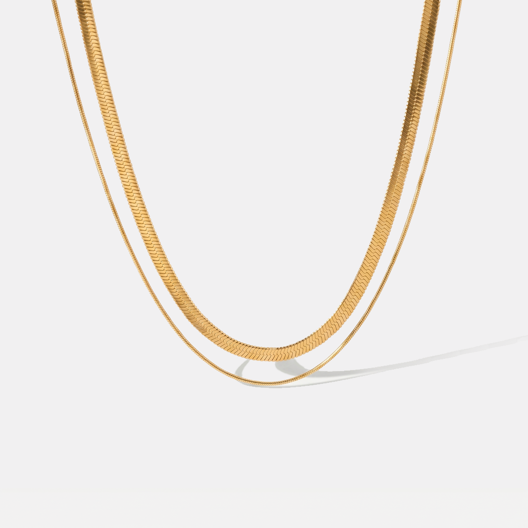 A layered gold-tone necklace of two flat herringbone chains, on a plain background