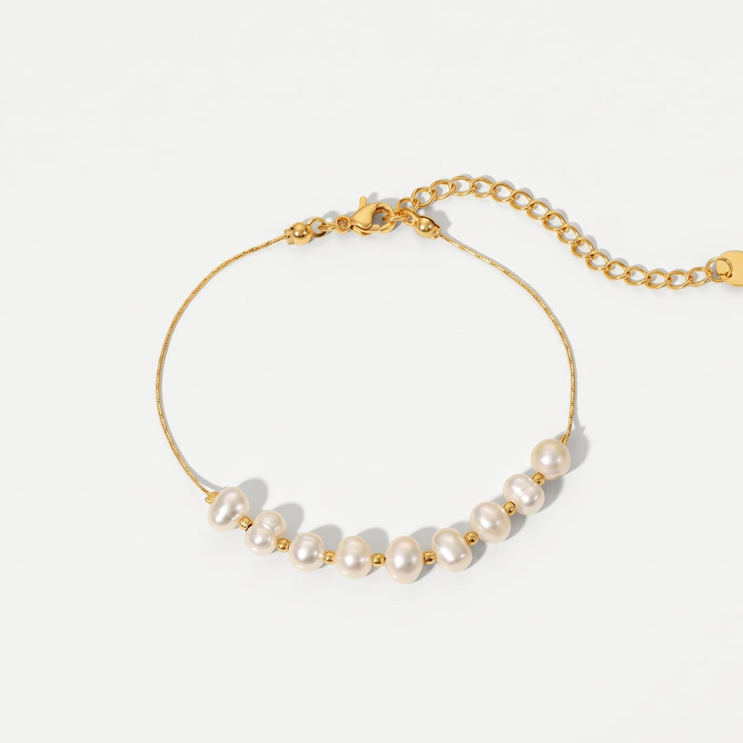 A fine gold-tone chain bracelet with a row of nine freshwater pearls, on a plain background