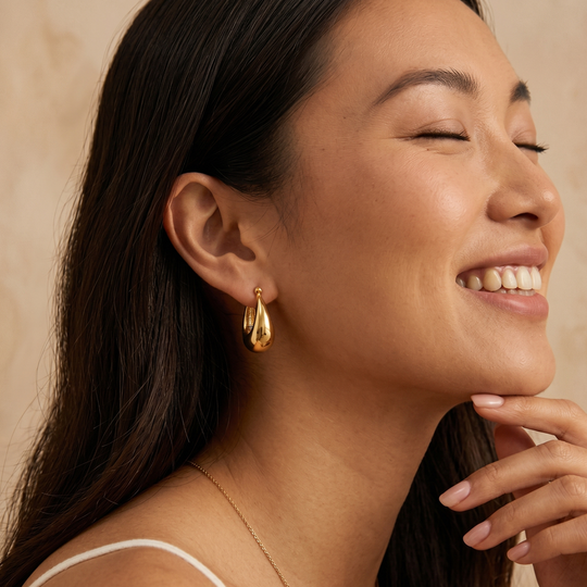 A gold-plated dome hoop earring worn, showing how the rounded hoop hangs from the lobe