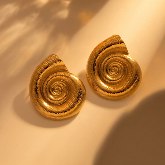 The pair of spiral shell studs resting on cream silk