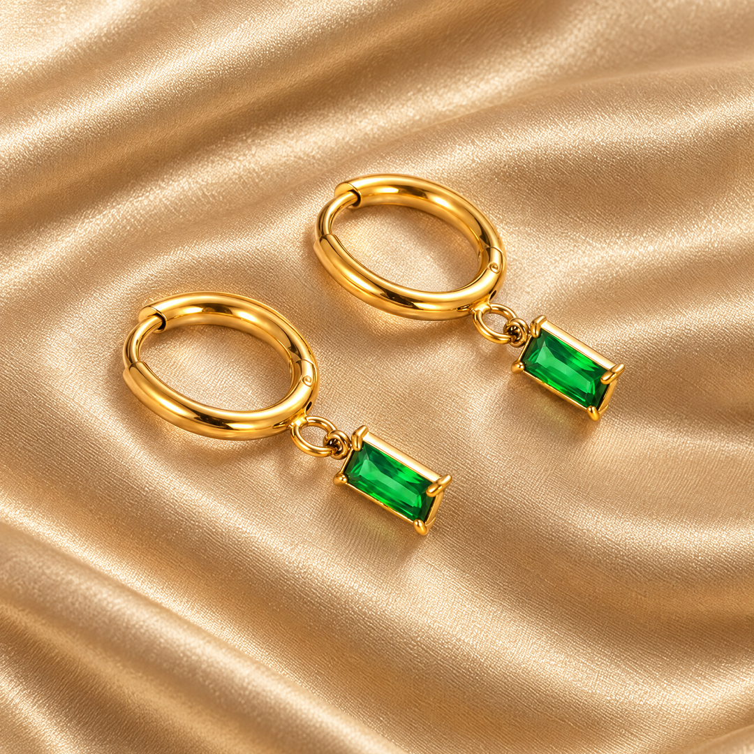 The Ines Green Drop Hoops resting on champagne satin