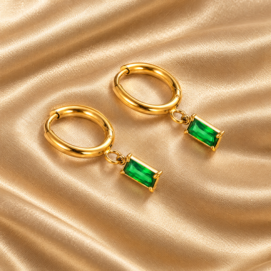 The Ines Green Drop Hoops resting on champagne satin