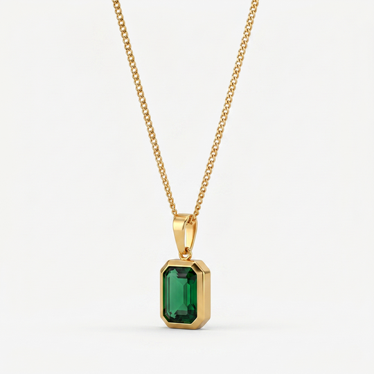 A gold-tone pendant necklace with a rectangular green crystal in a bezel, on a plain background
