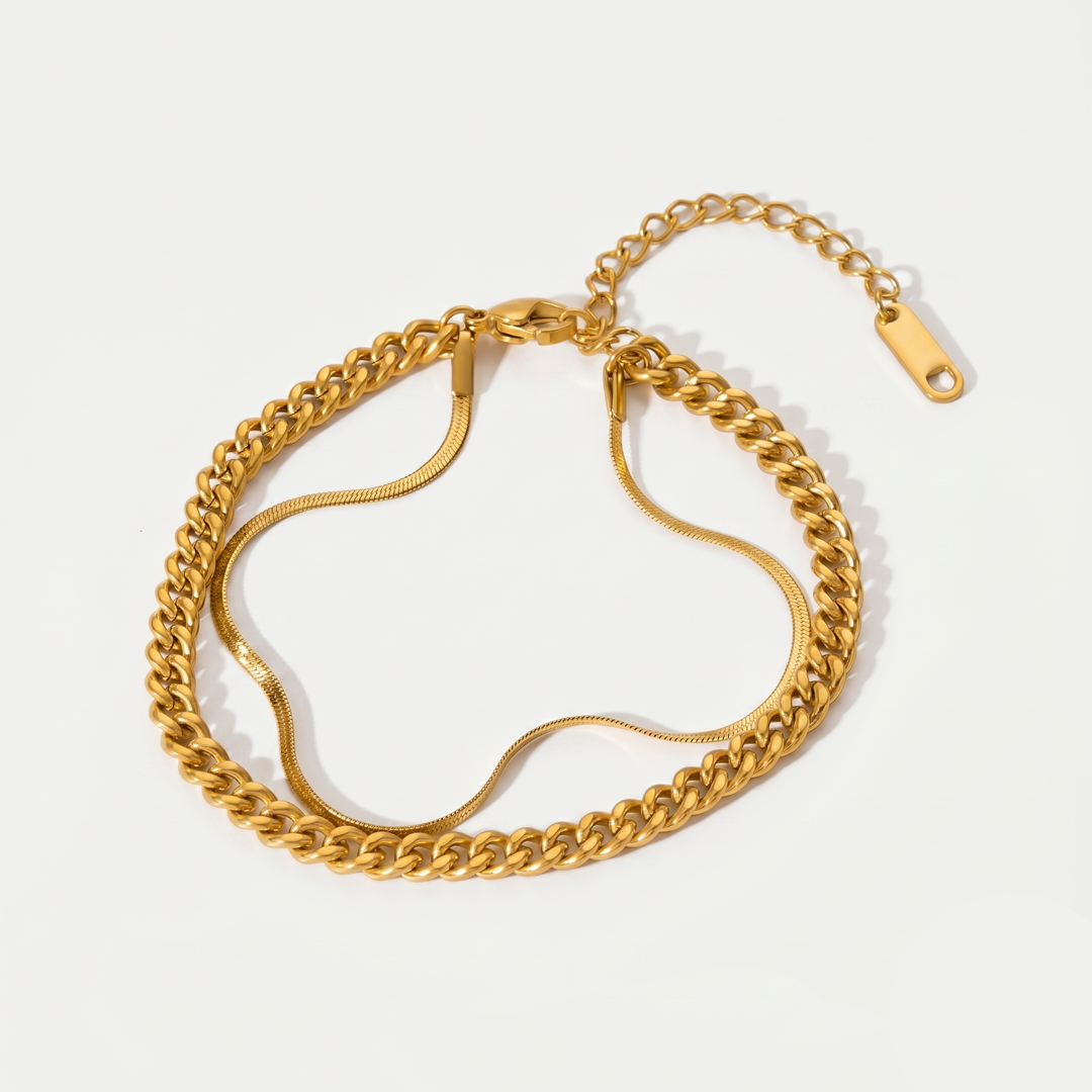A gold-tone layered bracelet of a curb chain and a snake chain on one clasp, on a plain background