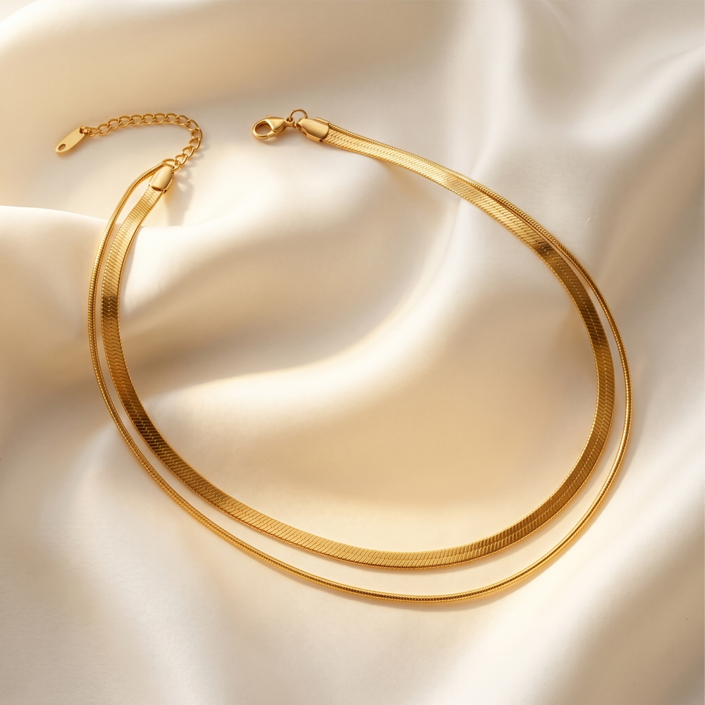 The two herringbone chains resting on cream silk, showing the clasp and extension