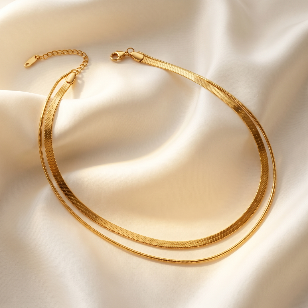 The two herringbone chains resting on cream silk, showing the clasp and extension