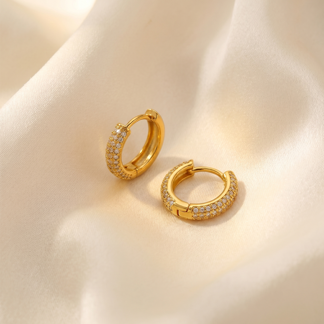 The pair of huggie hoops on cream silk, showing the hinged closure and the stones