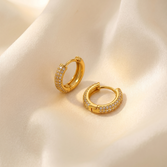 The pair of huggie hoops on cream silk, showing the hinged closure and the stones