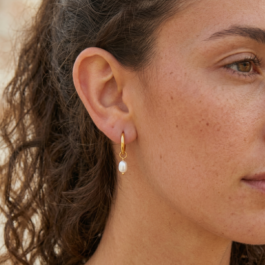 A gold-tone pearl hoop earring worn, showing how the hoop sits on the lobe and the pearl hangs just below it
