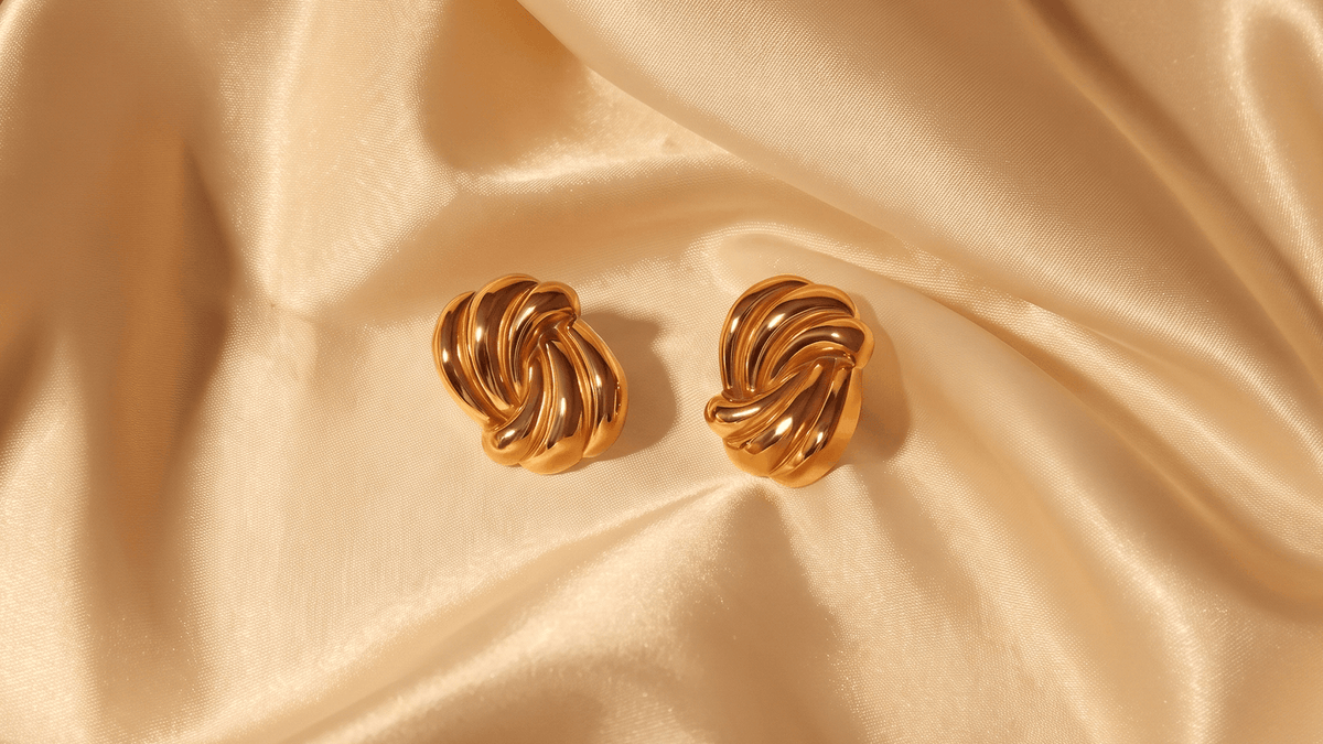 Gold-tone swirl stud earrings resting on champagne satin