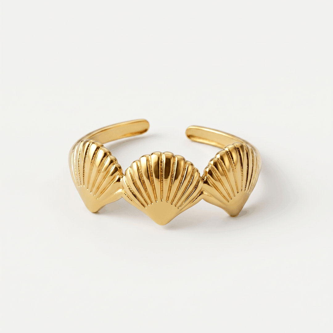 A gold-tone open ring with three ridged scallop shells, on a plain background