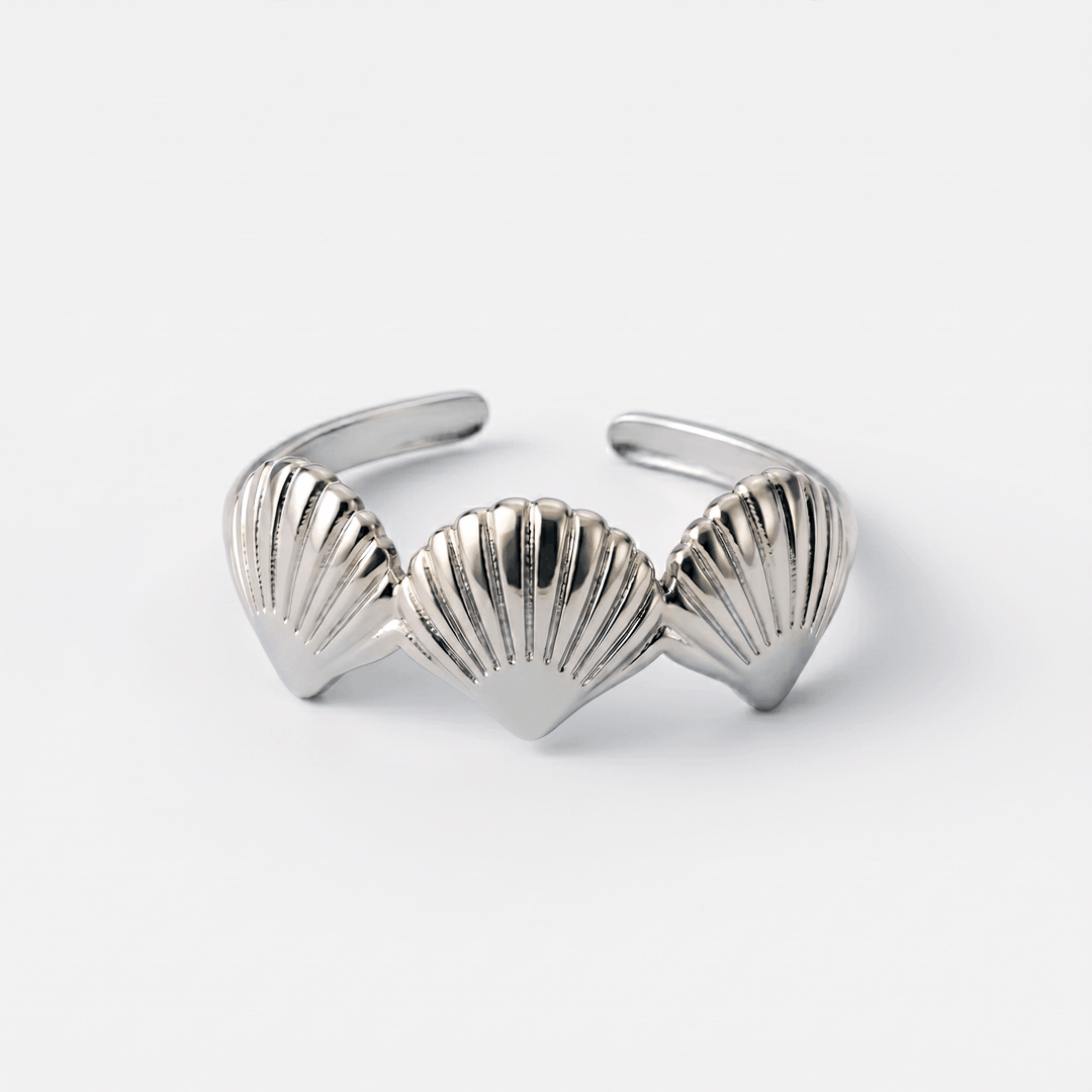 The scallop shell ring in silver-tone stainless steel, on a plain background