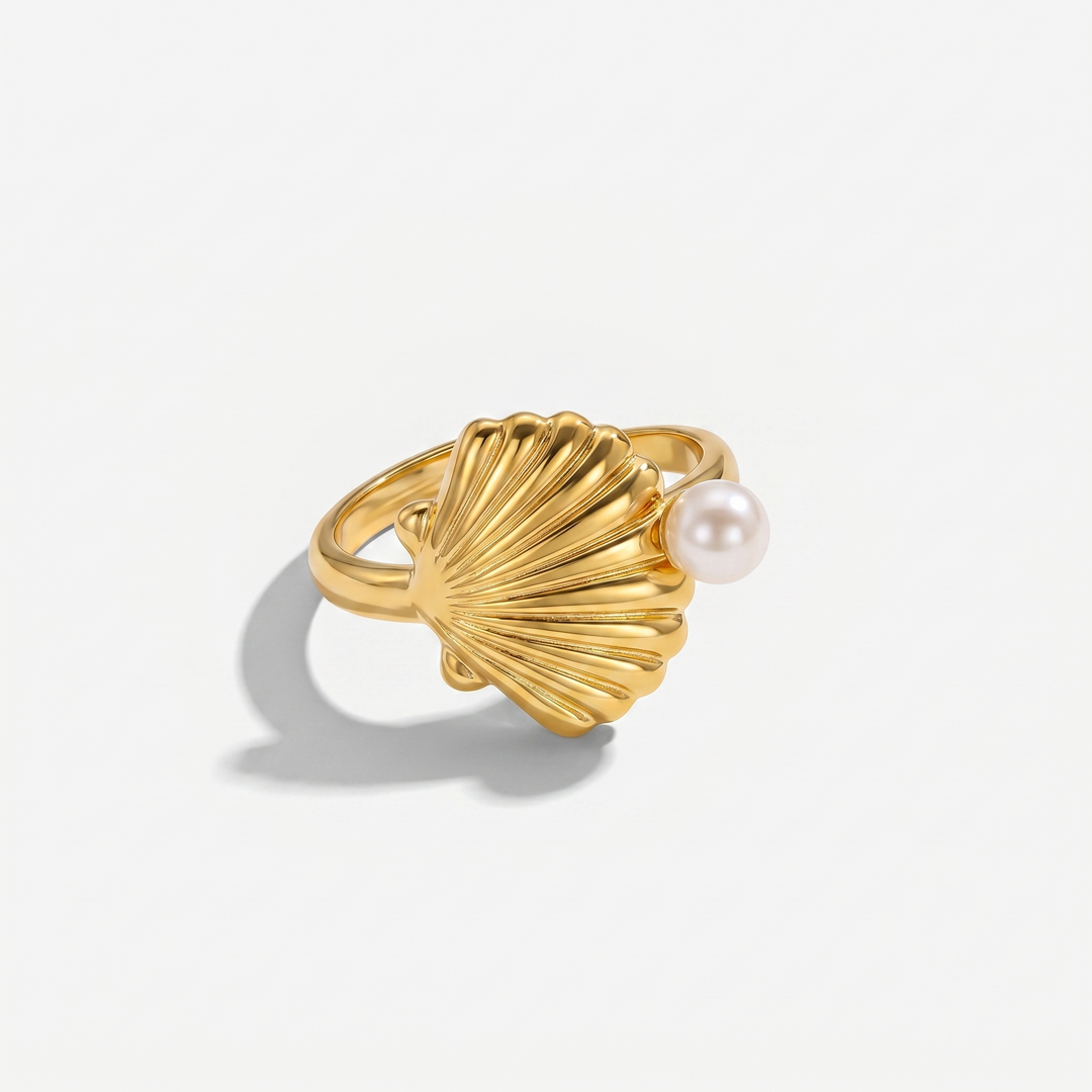 A gold-plated scallop shell ring with a small pearl at the edge, on a plain background