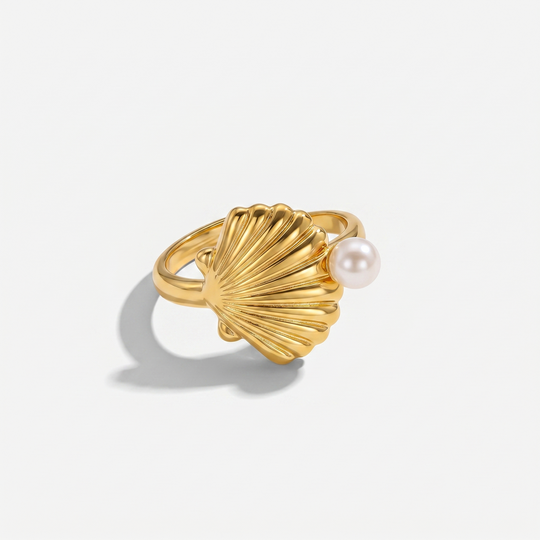 A gold-plated scallop shell ring with a small pearl at the edge, on a plain background