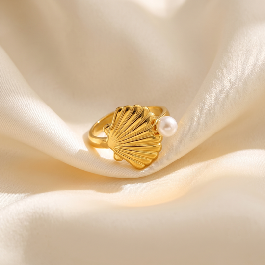 The shell ring resting on cream silk, showing the ridges and the pearl