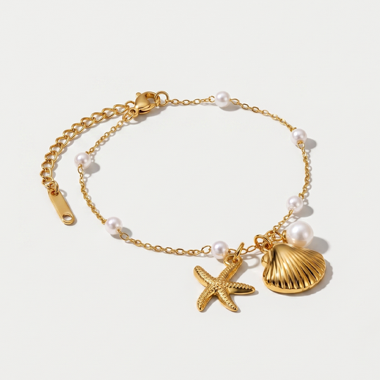 A gold-tone chain bracelet with a scallop shell, a starfish and small pearl stations, on a plain background