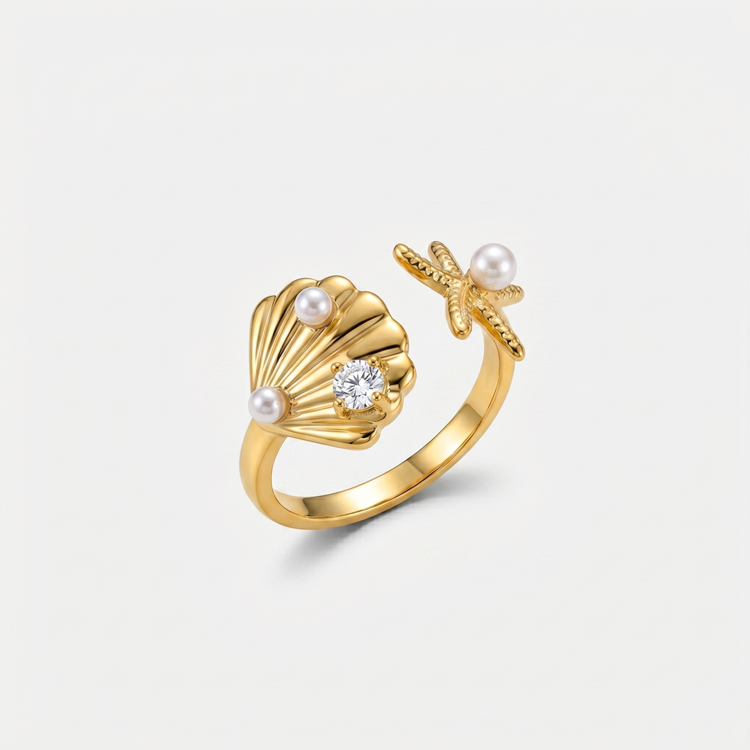 A gold-tone open ring with a scallop shell, a starfish and two small pearls, on a plain background