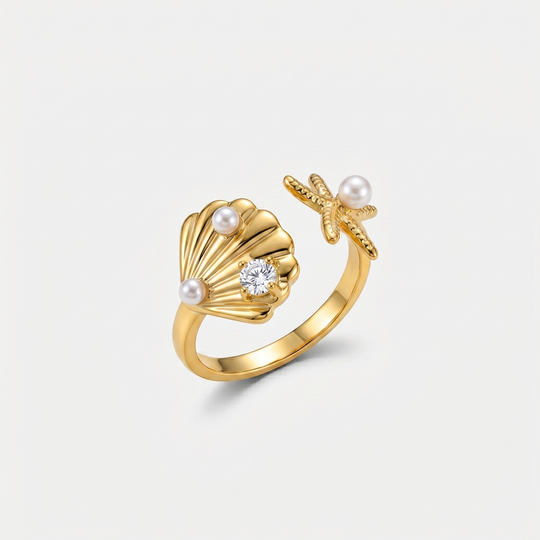 A gold-tone open ring with a scallop shell, a starfish and two small pearls, on a plain background