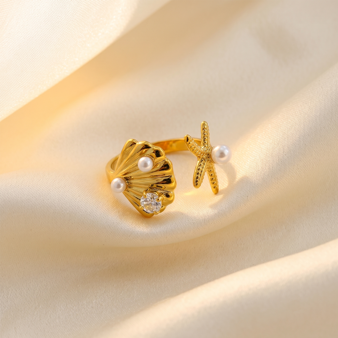 The shell and starfish ring resting on cream silk, showing the pearls and the crystal