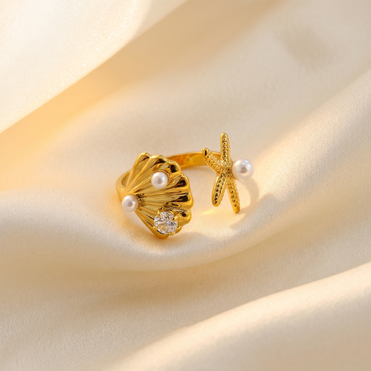 The shell and starfish ring resting on cream silk, showing the pearls and the crystal