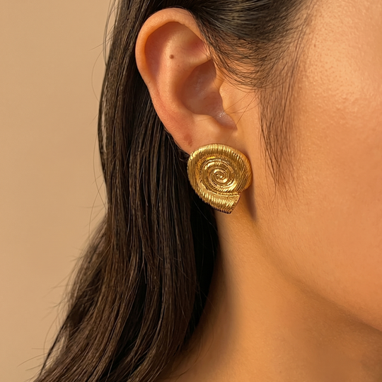 A gold-tone spiral shell stud worn, showing how it sits on the lobe