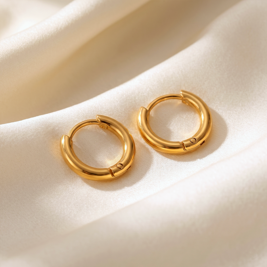 A pair of small gold-tone hoops resting on cream silk
