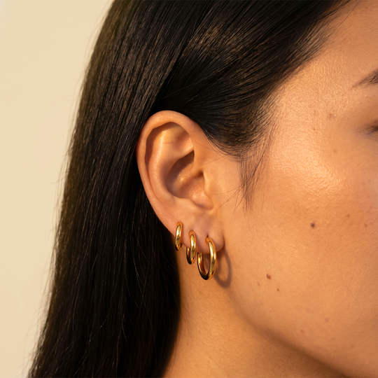 Close-up of three small gold-tone hoops worn in one ear, from the smallest at the top to the largest on the lobe
