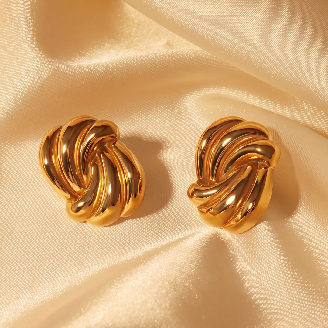 The pair of swirl studs resting on cream silk