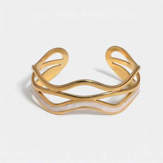 A gold-tone open cuff with three wave lines and a pearlescent white inlay, on a plain background
