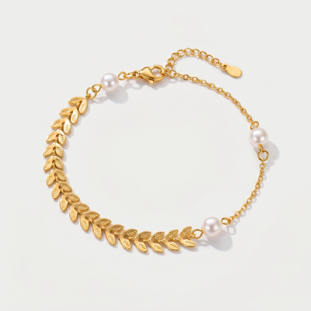 A gold-tone wheat-leaf chain bracelet with small pearl accents, on a plain background