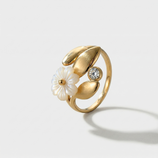 A gold-tone open ring with a white blossom among leaves and a crystal, on a plain background
